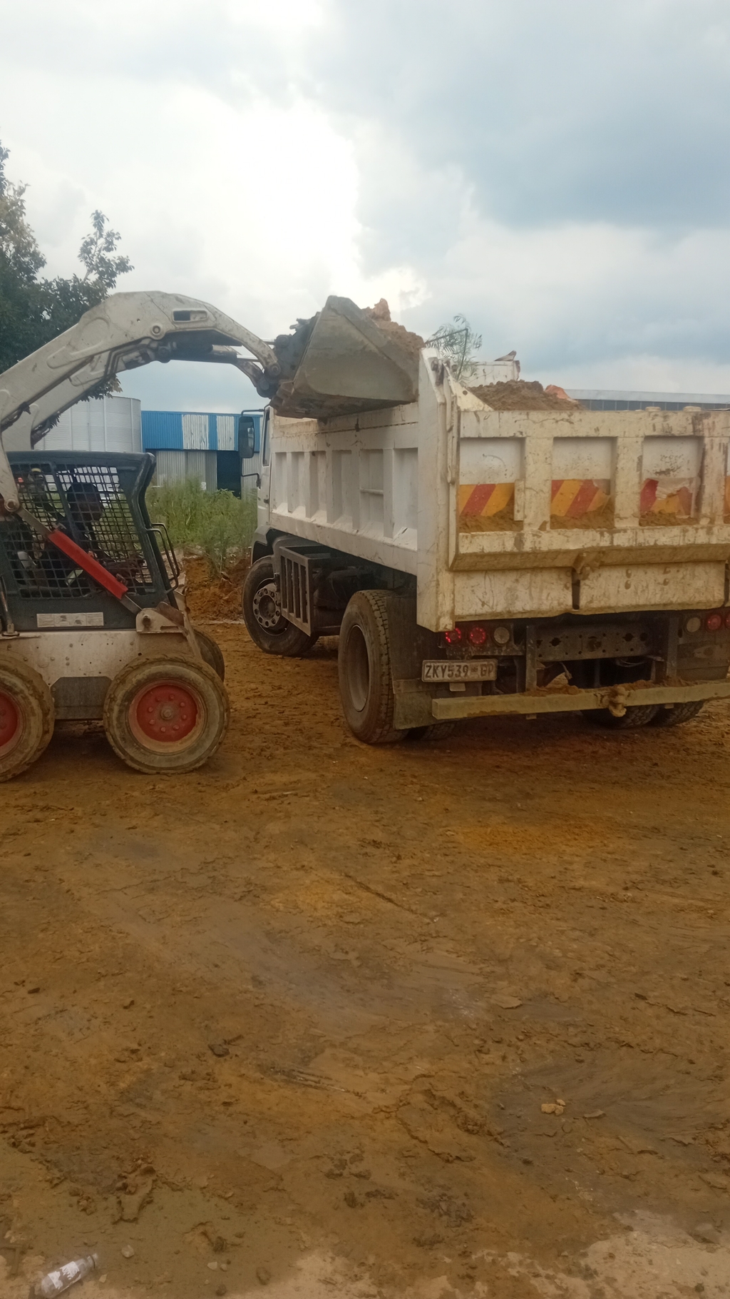 A Bob Cat machine loading a white truck of rubbles 