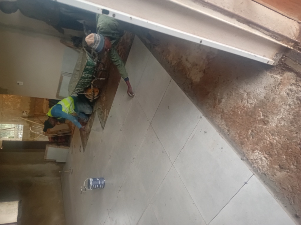 A man wearing a reflector jacket tiling the floor 